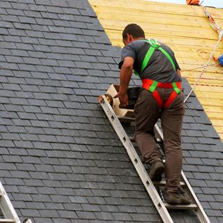 image of man on ladder putting shingles on new home
